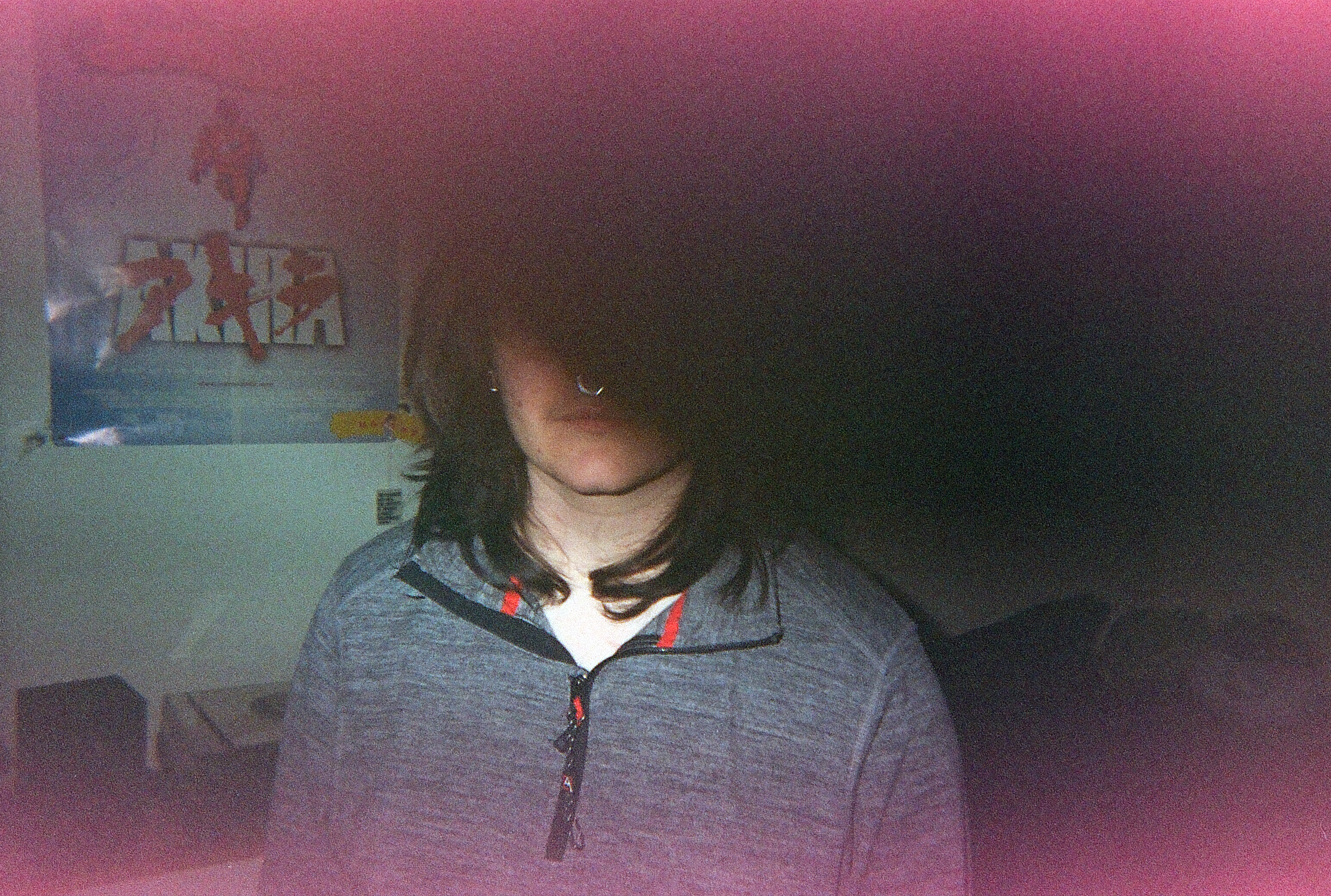 Film image of a white man with long, brown hair wearing a grey quarter-zip. A large shadow obscures the upper half of his face. The image has pink borders due to film expiration.